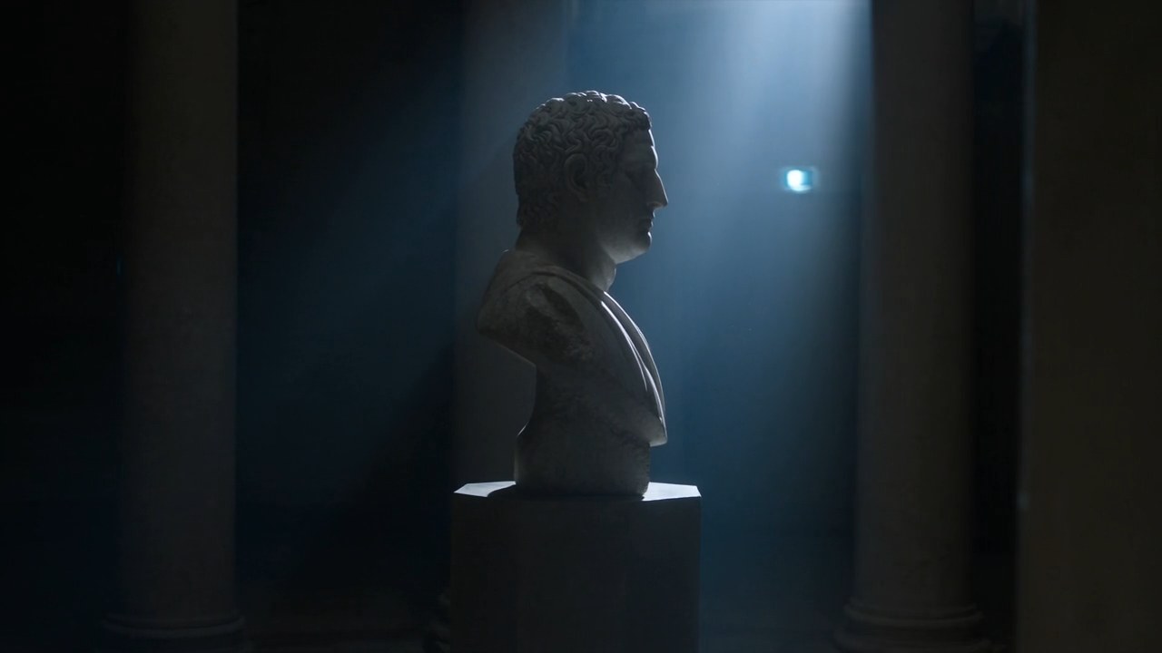 Fotogramma: un busto classico di marmo in una sala in penombra
